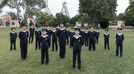 The Vienna Boys Choir standing outdoors at a park with a Ferris Wheel in the background