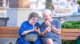 A man and woman sitting on an outdoor bench. They both are looking at the woman's phone.